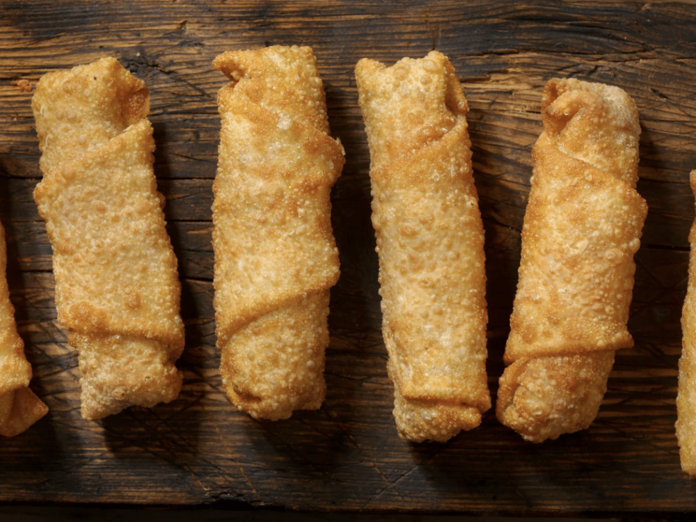 close up of several egg rolls lined up on a wood table